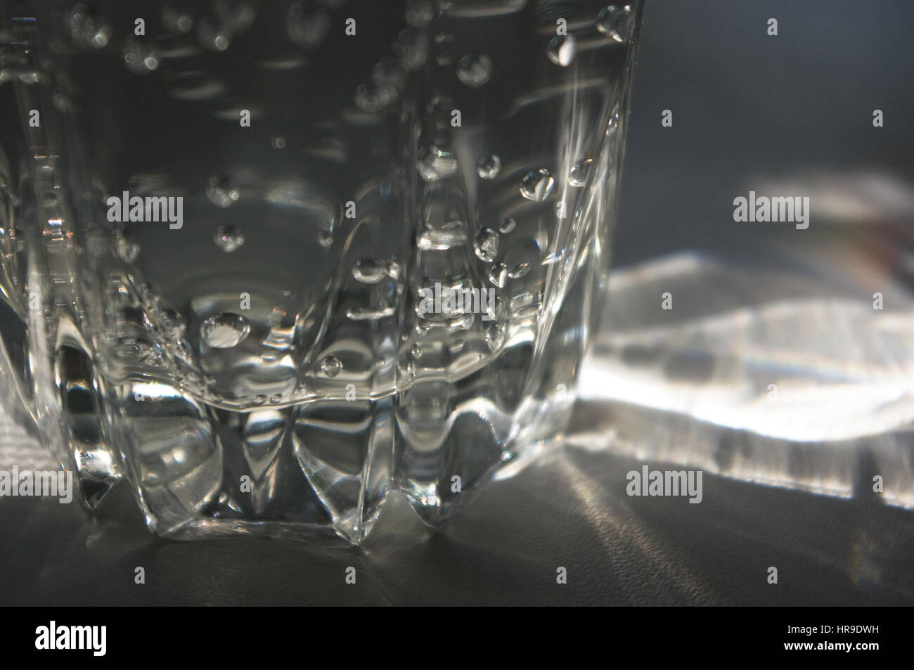 Vidrio Facetado transparente con agua burbujeante en el sol refracta la luz Foto de stock