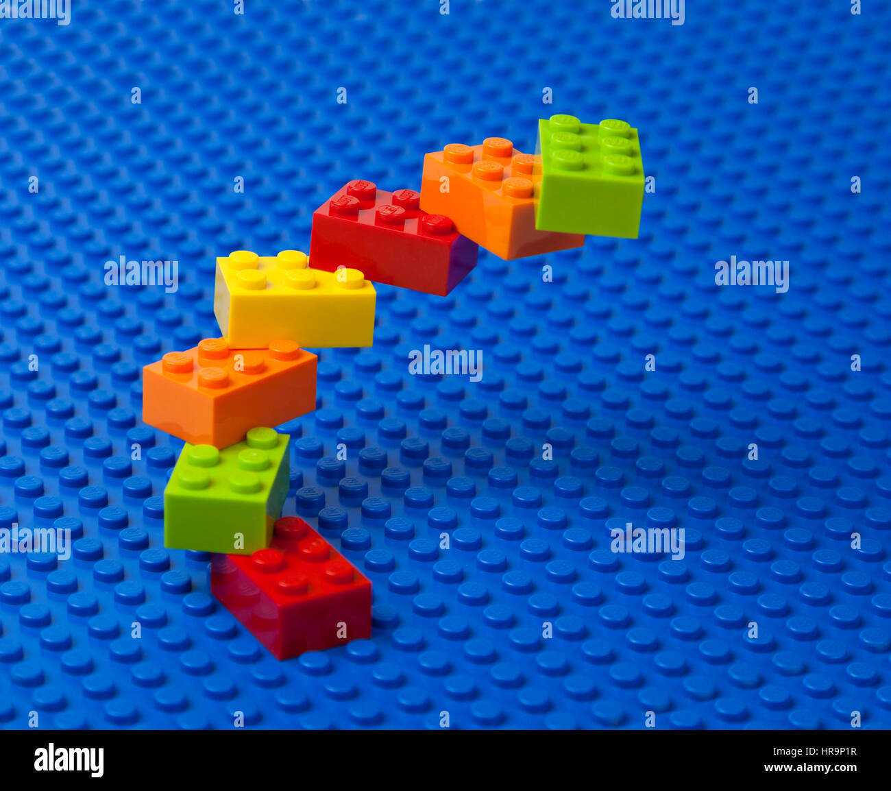 Espiral ascendente de escaleras o construcción de ladrillos LEGO entrelazados en una placa base de Lego azul. Foto de stock