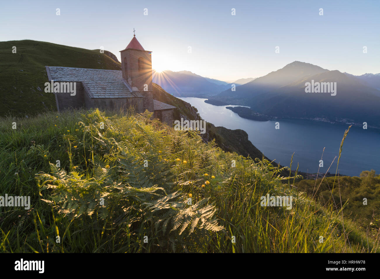 Sunbeam en la Iglesia de San Bernardo se ilumina el paisaje alrededor de las azules aguas del Lago Como al amanecer, Musso, Lombardía, Italia Foto de stock