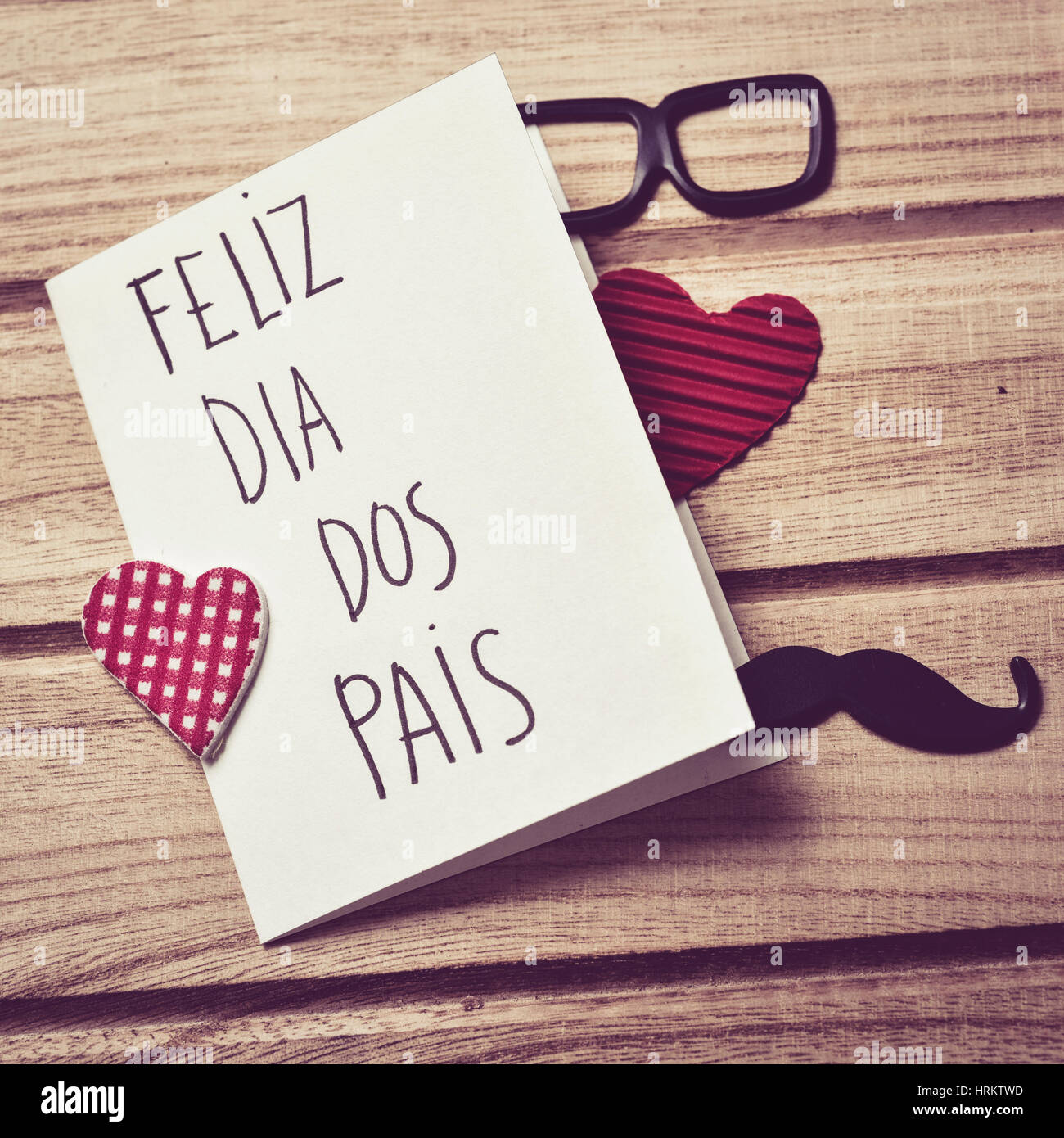 El texto feliz dia dos pais, feliz día del padre en portugués escrito en la  página de un bloc de notas, un par de anteojos negros, un bigote y algunos  él rojo