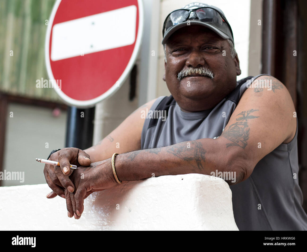 Hombre con bigote sosteniendo un cigarrillo. Un mal signo está detrás de él. Foto de stock