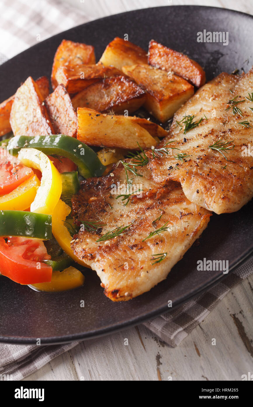 Filete de pescado blanco y rodajas de patata, ensalada fresca en un plato cerca. Vertical Foto de stock