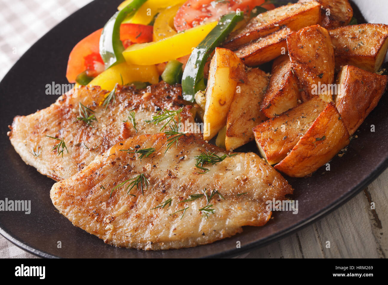 Filete de pescado blanco y rodajas de patata, ensalada fresca en una placa horizontal cerca. Foto de stock