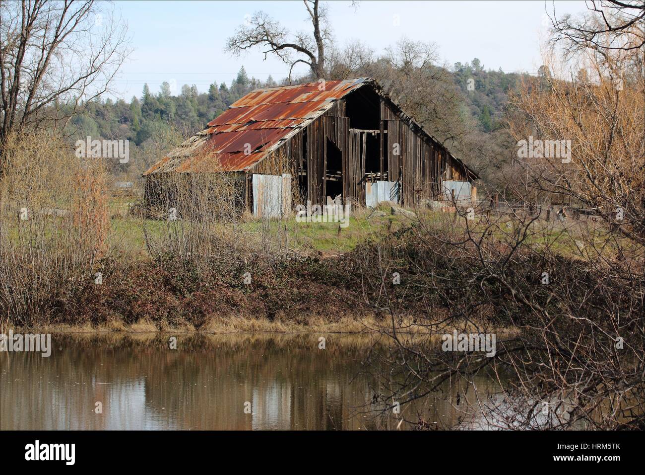La superficie lisa de un estanque situado en Somerset, California, refleja un antiguo granero de madera que está cerca del agua, EE.UU. Foto de stock