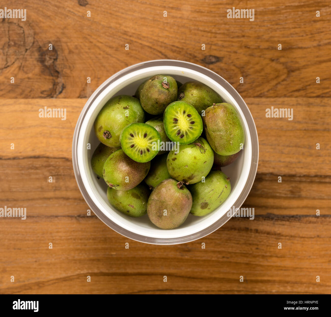 Antena o vista superior de un tazón de vidrio blanco kiwiberry orgánica con una fruta cortada en dos y sentado en la superficie de la mesa de madera vieja Foto de stock