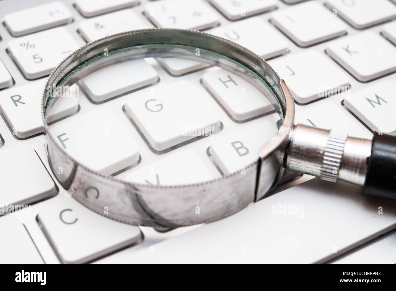 Lente de mano en un teclado, concepto de búsqueda en internet Foto de stock