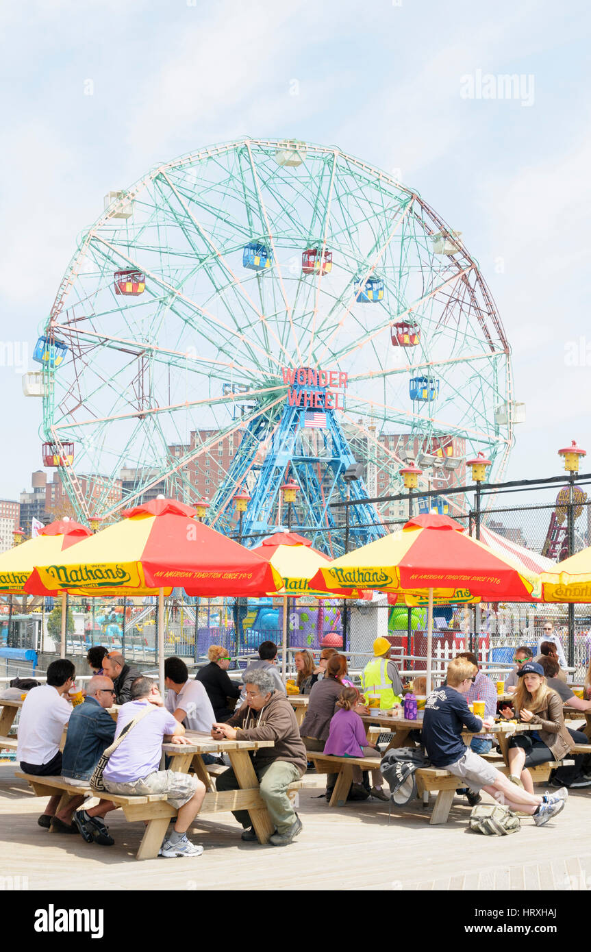 Gente comiendo delante de la rueda de maravilla, deno's Amusement Park, Coney Island, Brooklyn, Nueva York, EE.UU. Foto de stock