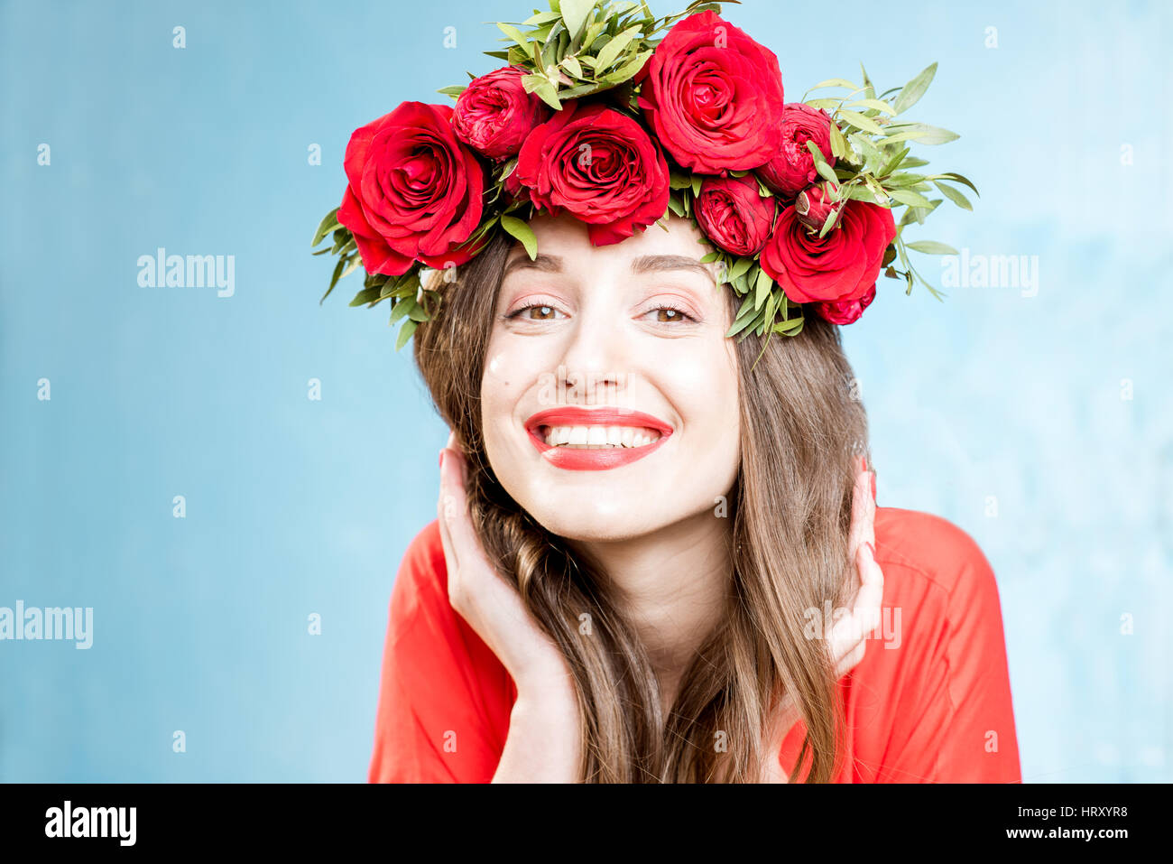 Colorido retrato de una mujer hermosa en el vestido rojo con corona de rosas  rojas sobre el fondo azul Fotografía de stock - Alamy