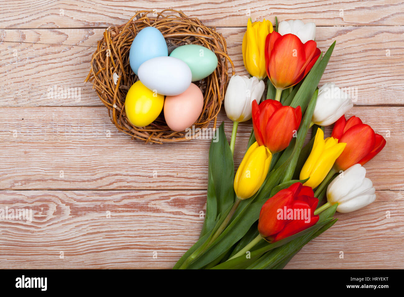 Los huevos de Pascua en un nido de aves con coloridos tulipanes sobre fondo de madera Foto de stock