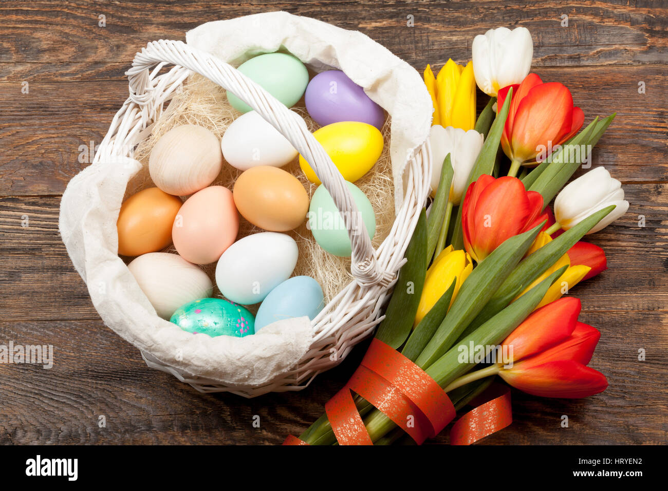 Los huevos de pascua en una cesta con coloridos tulipanes blancos sobre fondo de madera Foto de stock