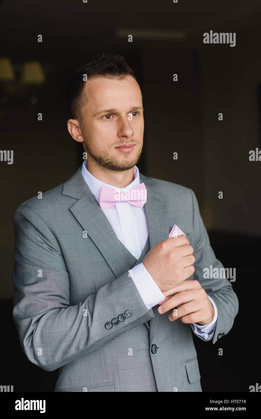 Elegante moda joven hombre vestirse para la celebración de bodas. Hermoso  vestidos de novio moderno traje gris, camisa blanca y corbata rosa  preparándose Fotografía de stock - Alamy