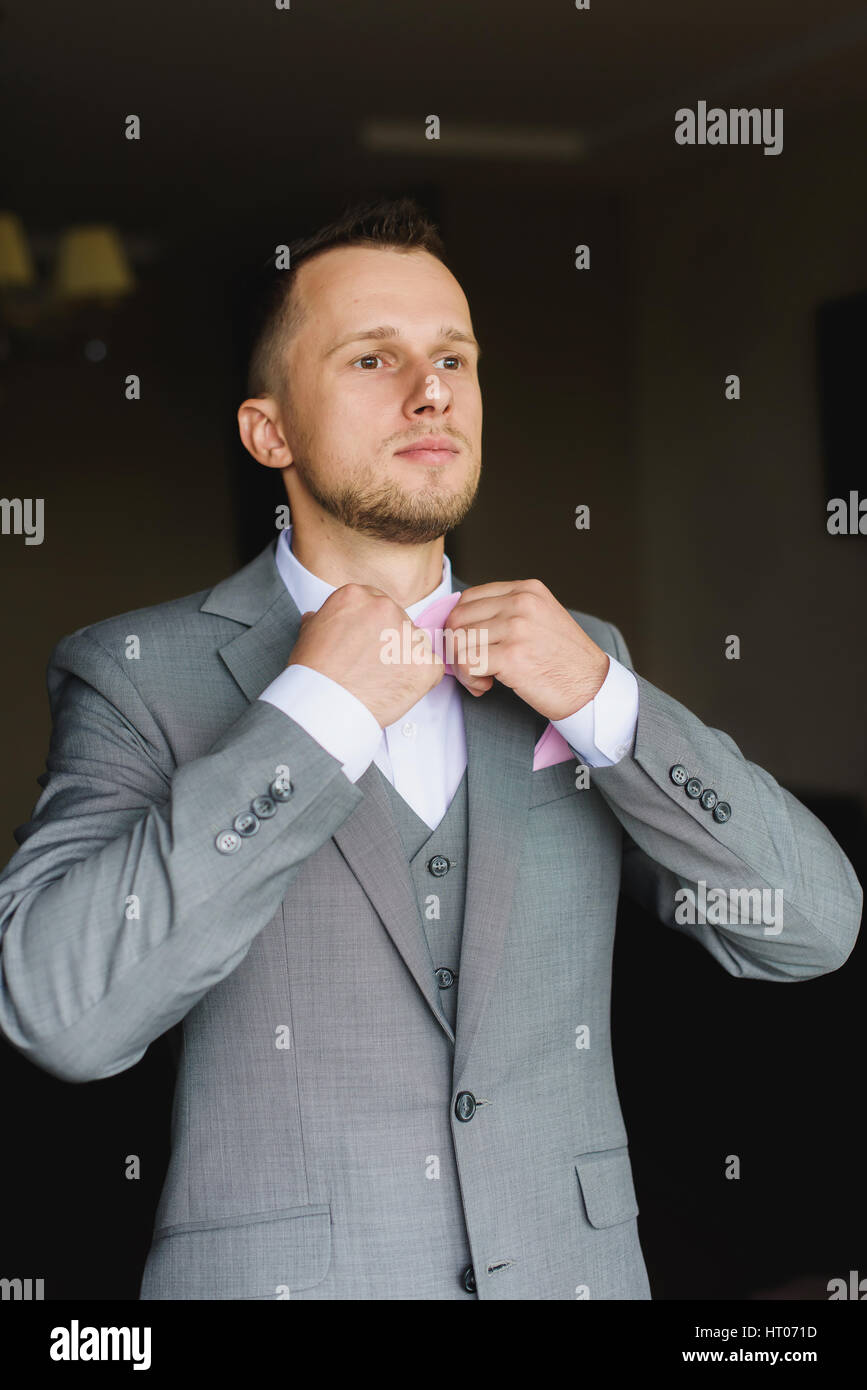 Elegante moda joven hombre vestirse para la celebración de bodas. Hermoso  vestidos de novio moderno traje gris, camisa blanca y corbata rosa  preparándose Fotografía de stock - Alamy