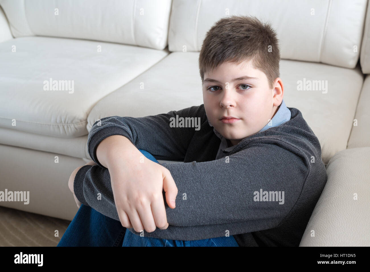 13 años de muchacho sentado cerca del sofá en la habitación Foto de stock