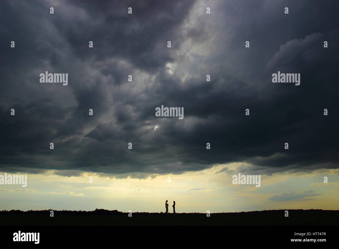 Personas de remolque en el horizonte, bajo el cielo tormentoso en Back light Foto de stock