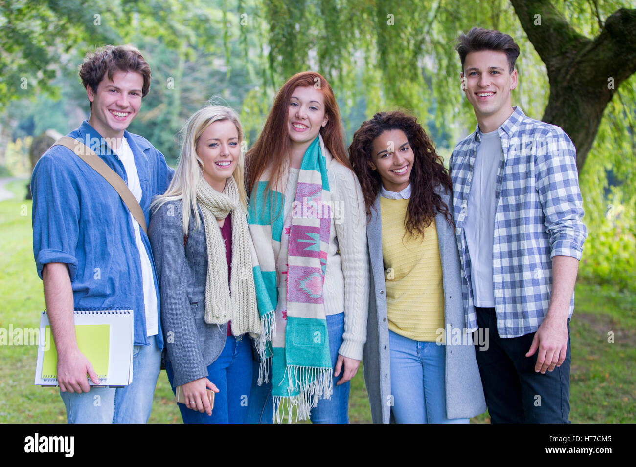 Un grupo multiétnico de estudiantes adolescentes que sonreír a la cámara, ya que posan para una fotografía en el exterior. Están envueltos caliente durante el invierno und permanente Foto de stock