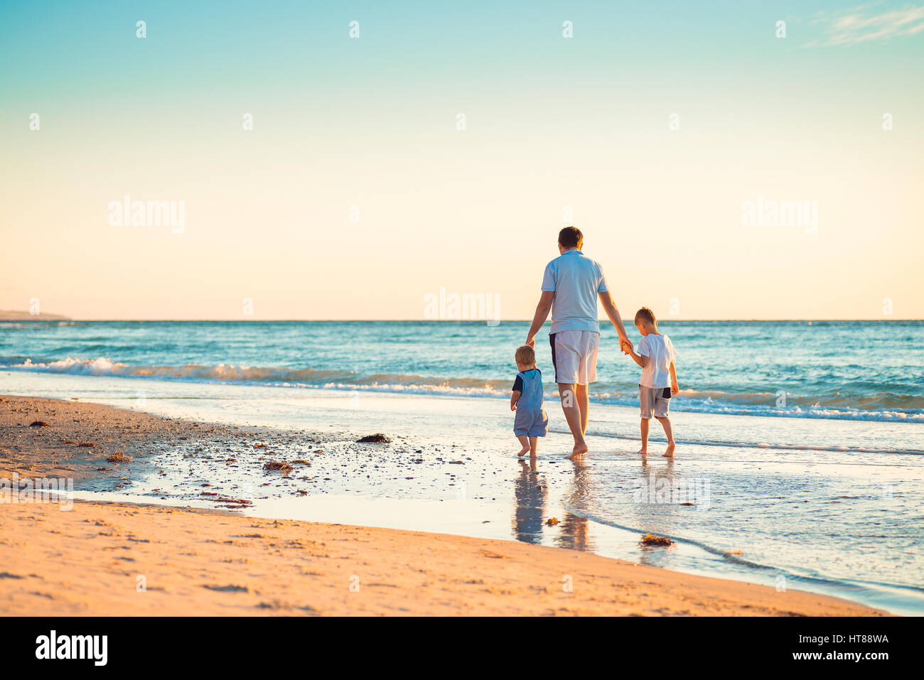 Padre de dos hijos, caminar en la playa y tomados de la mano Foto de stock
