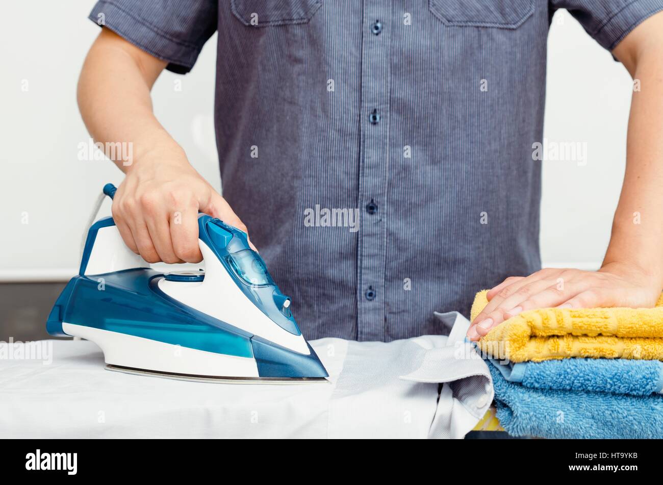 El hombre plancha la ropa sobre la tabla de planchar con vapor de hierro  azul Fotografía de stock - Alamy