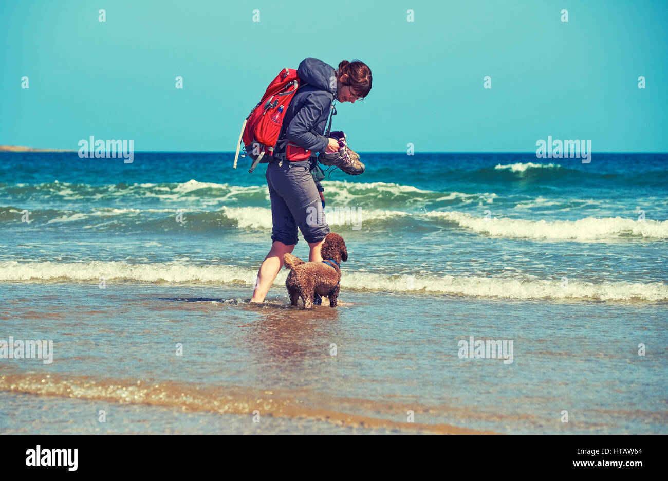 Un caminante y su perro jugando en una soleada playa de arena. Embleton Bahía, Inglaterra. Color de grano y estilo aplicado. Foto de stock