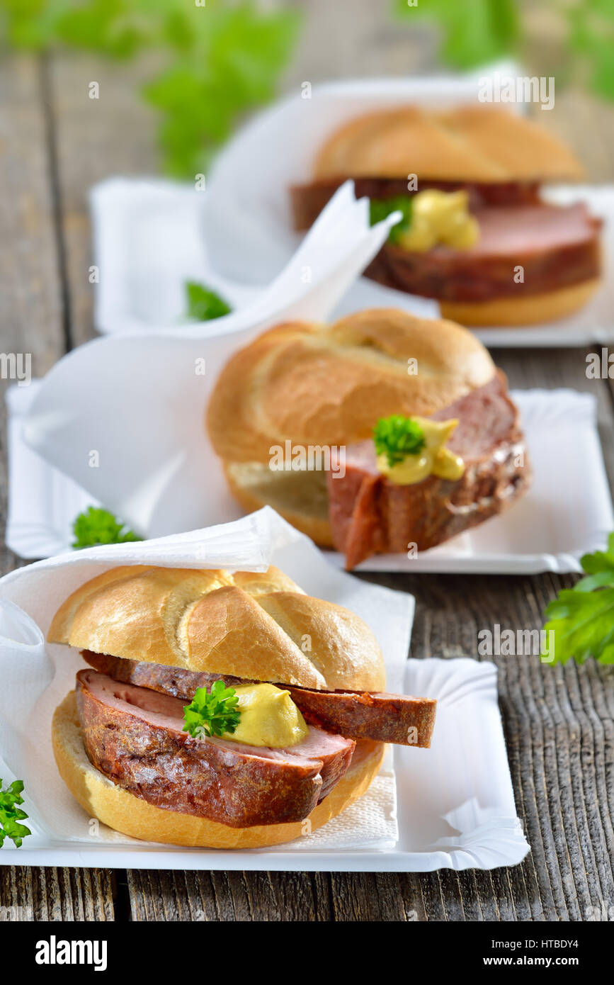 Comida para llevar de Baviera: Tres rodillos con pan de carne cocida y mostaza en platos de papel Foto de stock