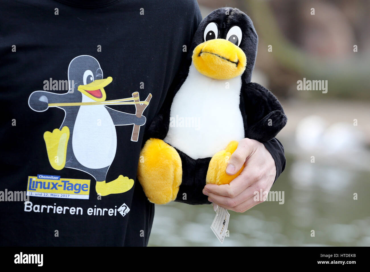 Un hombre parado con una camiseta y un muñeco de peluche de la mascota de  Linux, el pingüino Tux, durante una conferencia de prensa en el Tierpark en  Limbach-Oberfrohna, Alemania, el 10