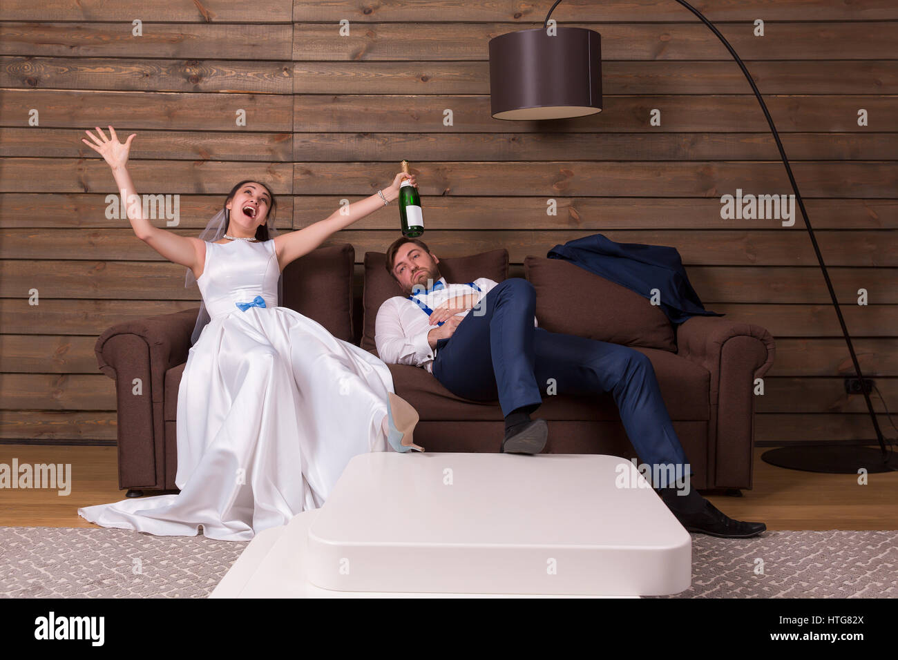 Novia borracho con la botella de alcohol y el novio durmiendo en cama después de la boda. Interior de la sala de madera sobre antecedentes Foto de stock