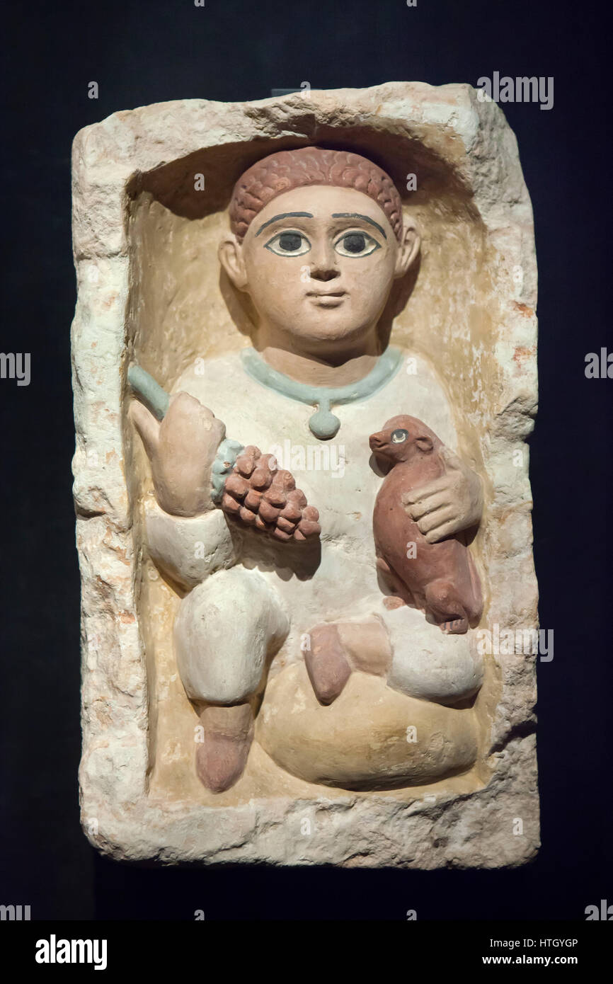 El niño con un racimo de uvas y un perro pequeño. Tumba de piedra caliza copta estela de Antinopolis, siglo IV d.C., en exhibición en el Museo Staatliches Agyptischer Kunst (Museo Estatal de Arte Egipcio) en Munich, Baviera, Alemania. Foto de stock