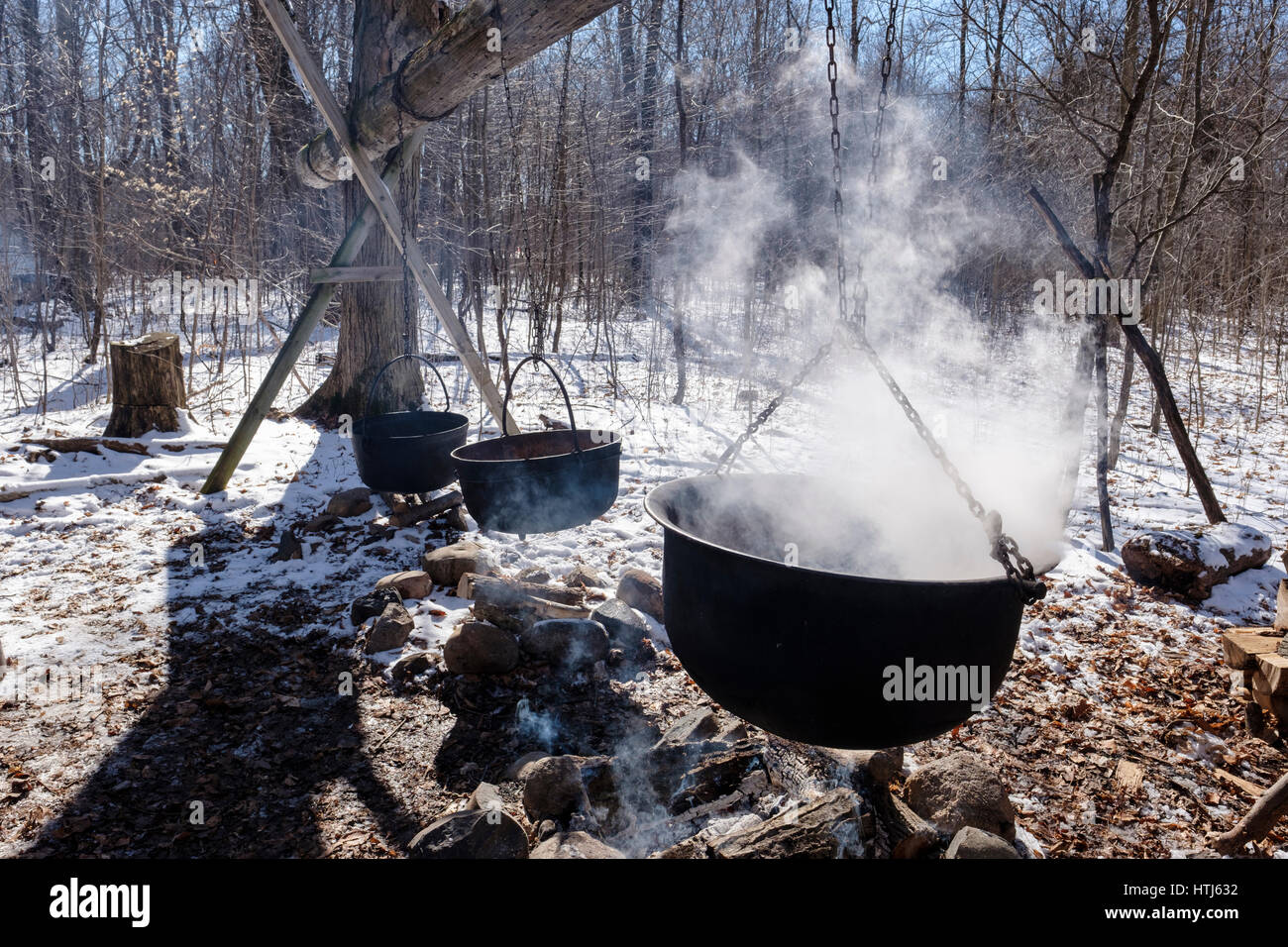 Tres ollas de hierro fundido negro, calderos, buques, pende sobre el fuego para hervir sap para producir el jarabe de arce en una granja de producción de jarabe de arce de azúcar / Bush. Foto de stock