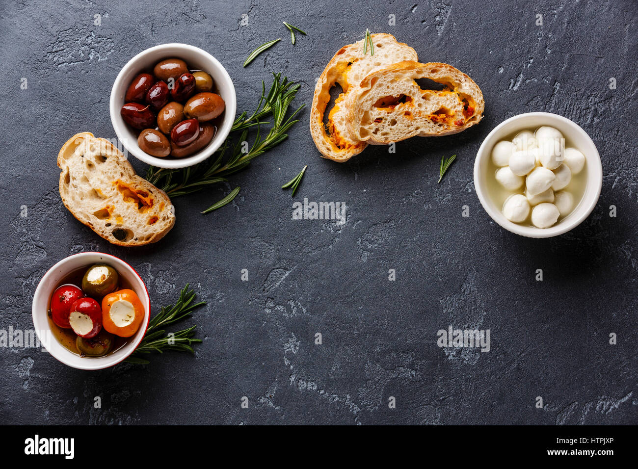 Aceitunas, pimientos rellenos, mini queso Mozzarella y rodajas de pan ciabatta sobre fondo oscuro espacio de copia Foto de stock