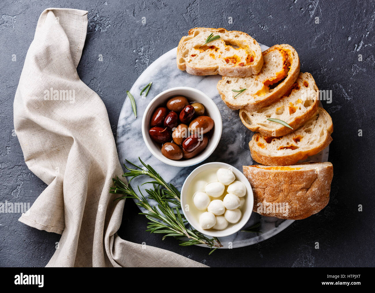 Aceitunas, mini queso Mozzarella y rodajas de pan ciabatta con queso sobre fondo oscuro Foto de stock