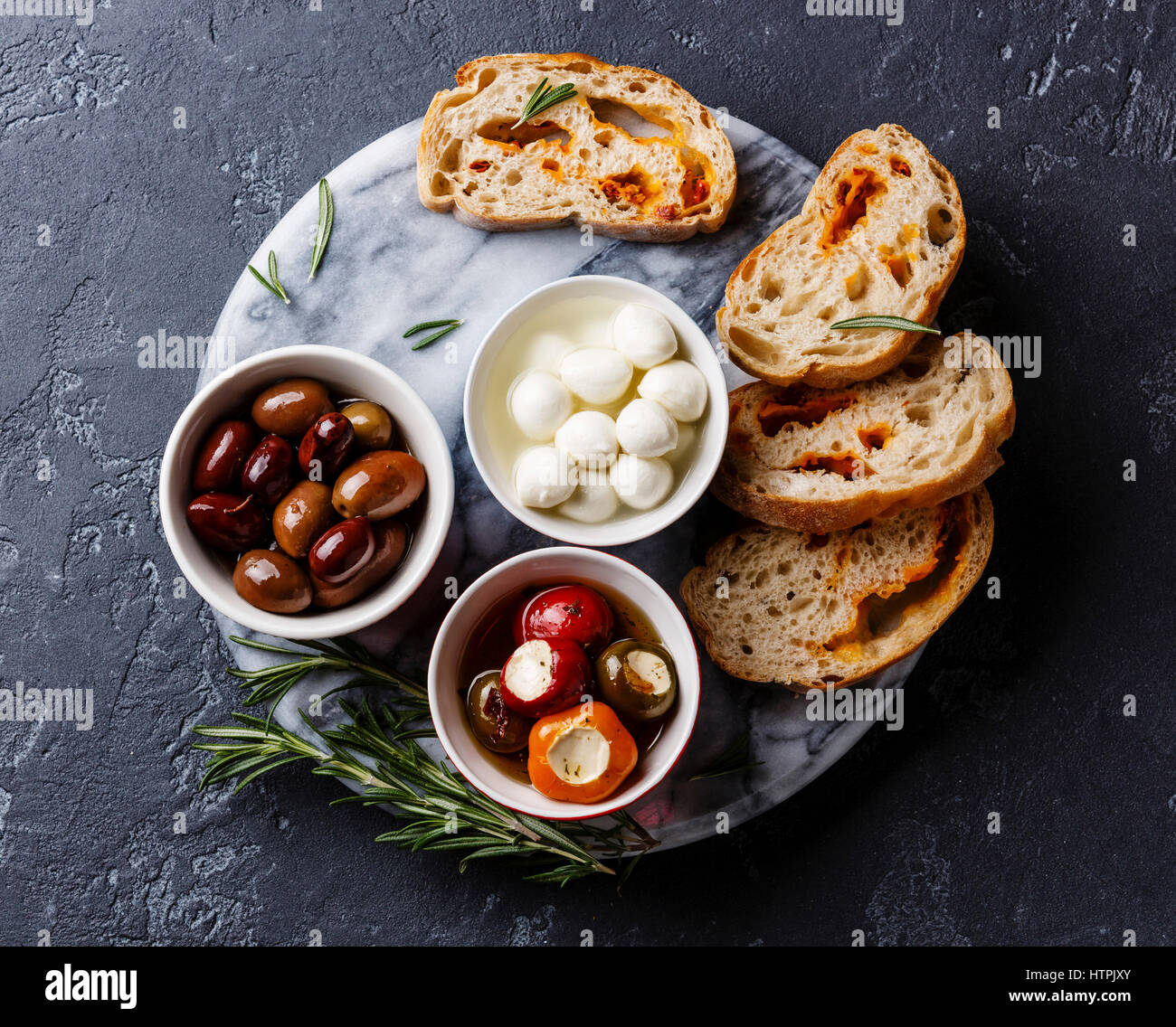 Aceitunas, pimientos rellenos, mini queso Mozzarella y rodajas de pan ciabatta sobre fondo oscuro Foto de stock