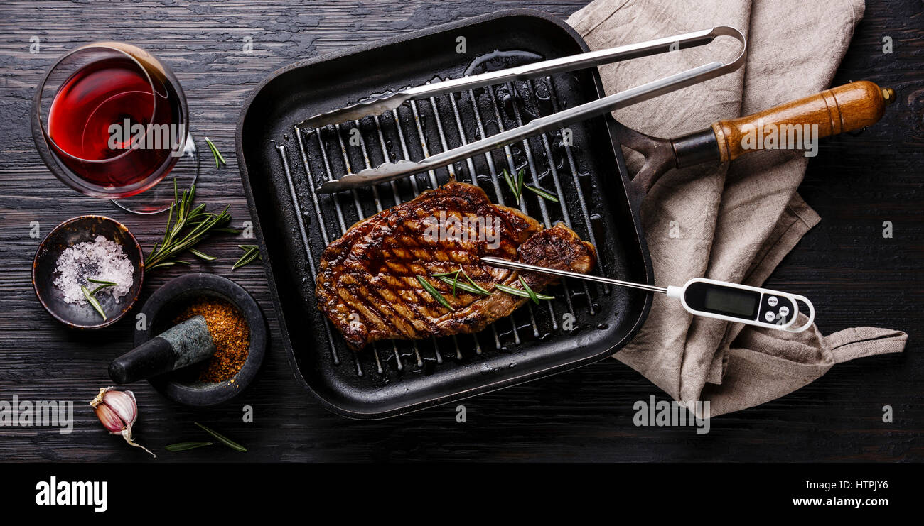 El solomillo de carne a la parrilla sobre la cacerola y termómetro de carne negra sobre fondo de madera quemada Foto de stock
