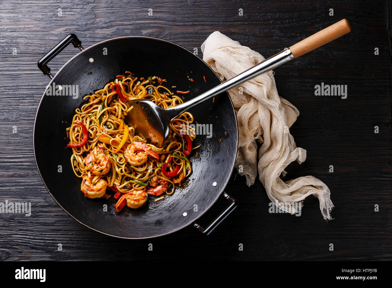 Udon fideos salteados con langostinos y camarones verduras en wok pan negro sobre fondo de madera quemada Foto de stock