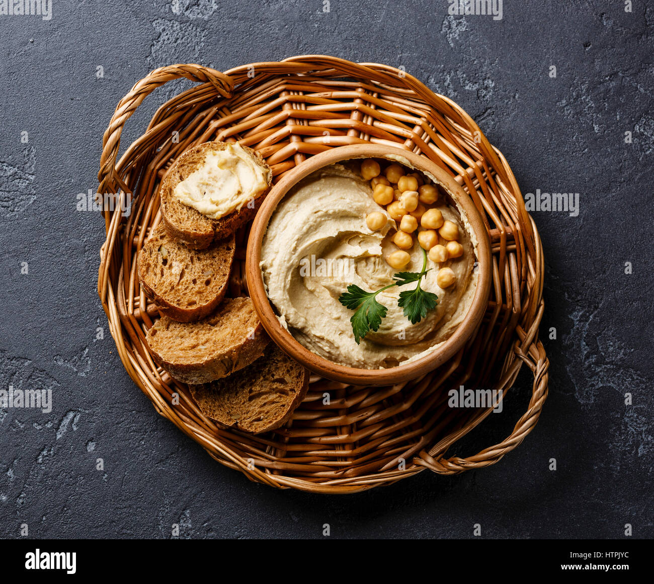 Hummus y pan casero en Bandeja mimbre sobre fondo de piedra negra Foto de stock