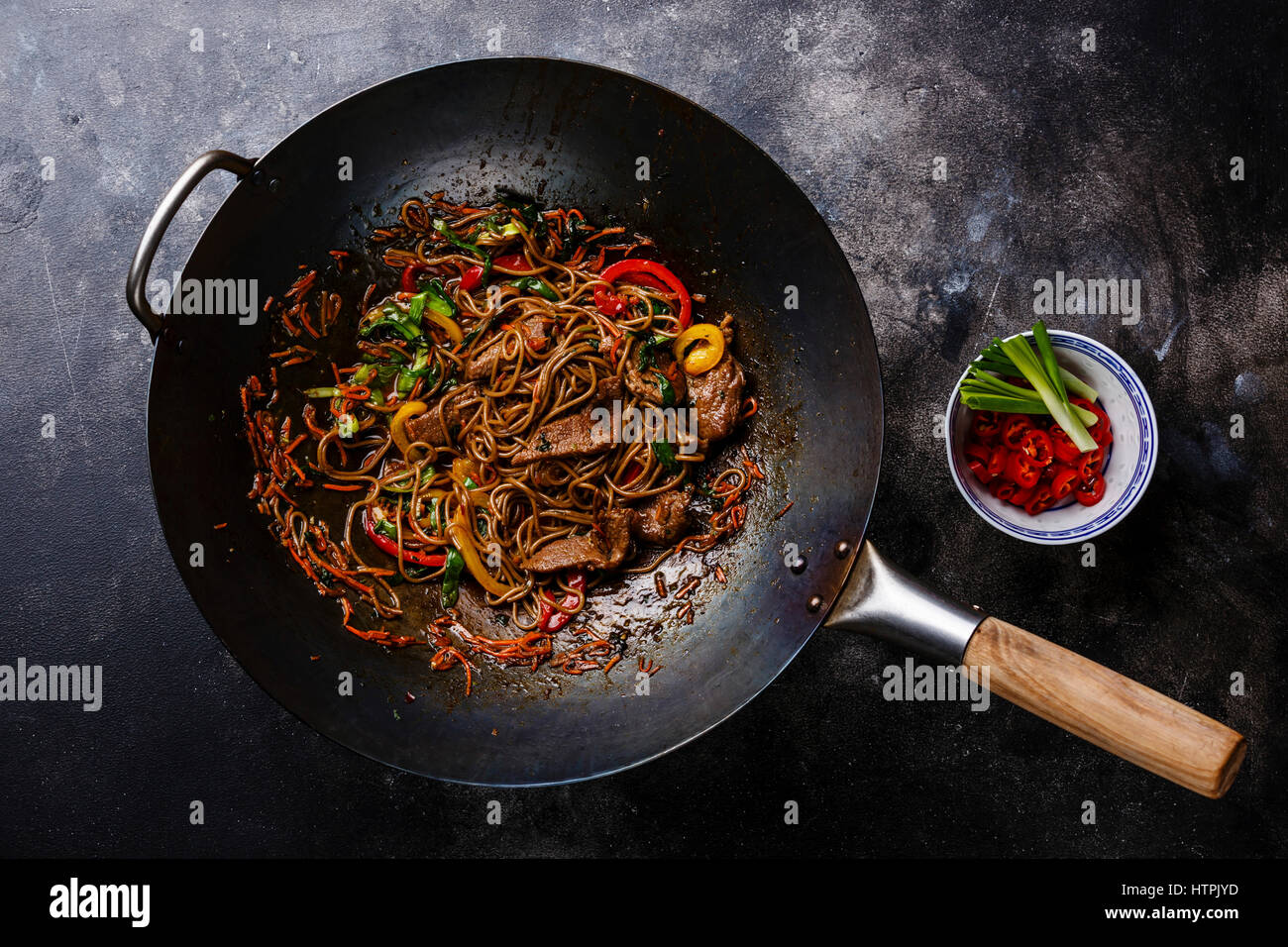 Salteado de fideos soba con la carne y verduras en wok pan sobre fondo oscuro Foto de stock