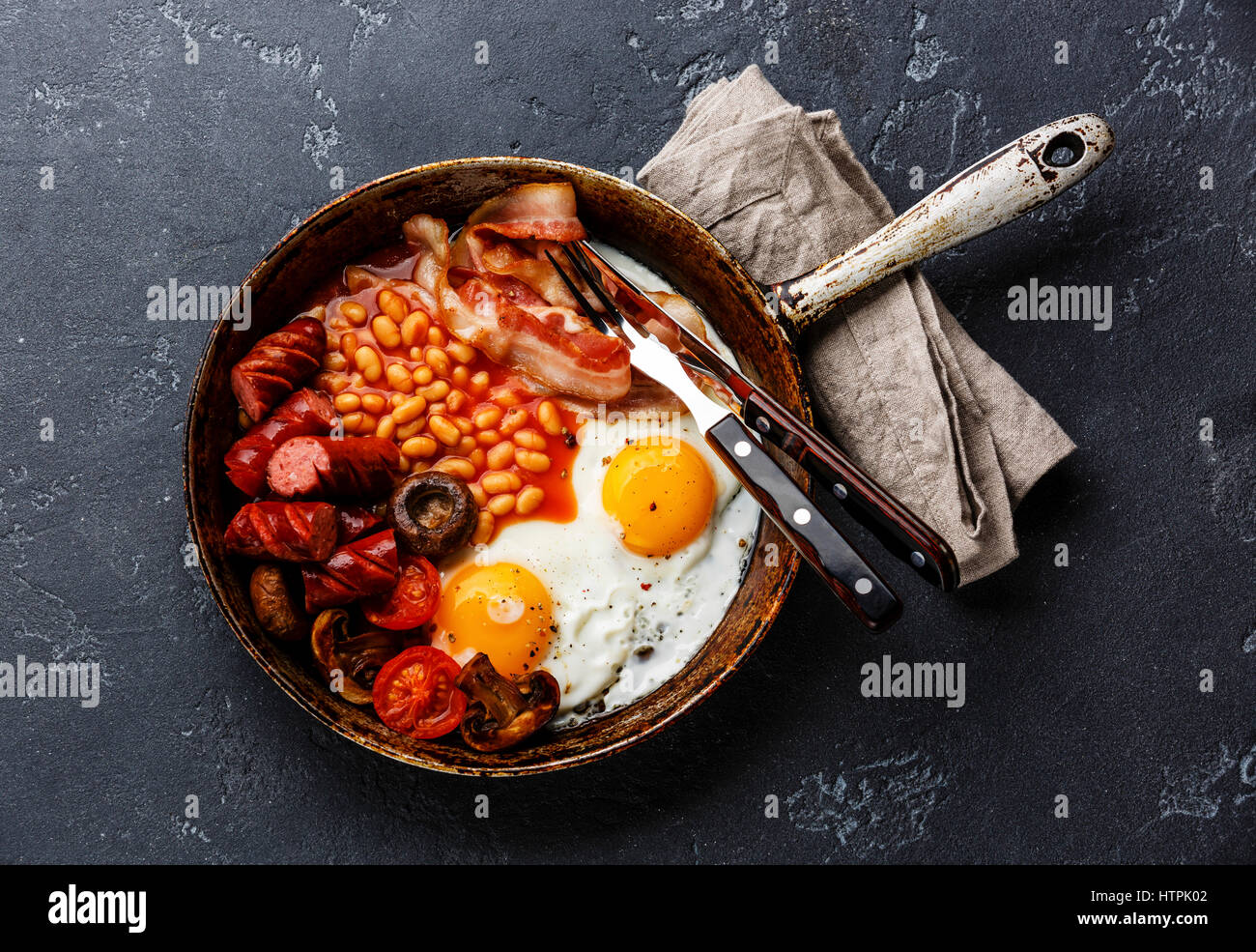 Desayuno inglés en sartén con huevos fritos, salchichas, tocino y frijoles en piedra oscura espacio copia de fondo Foto de stock