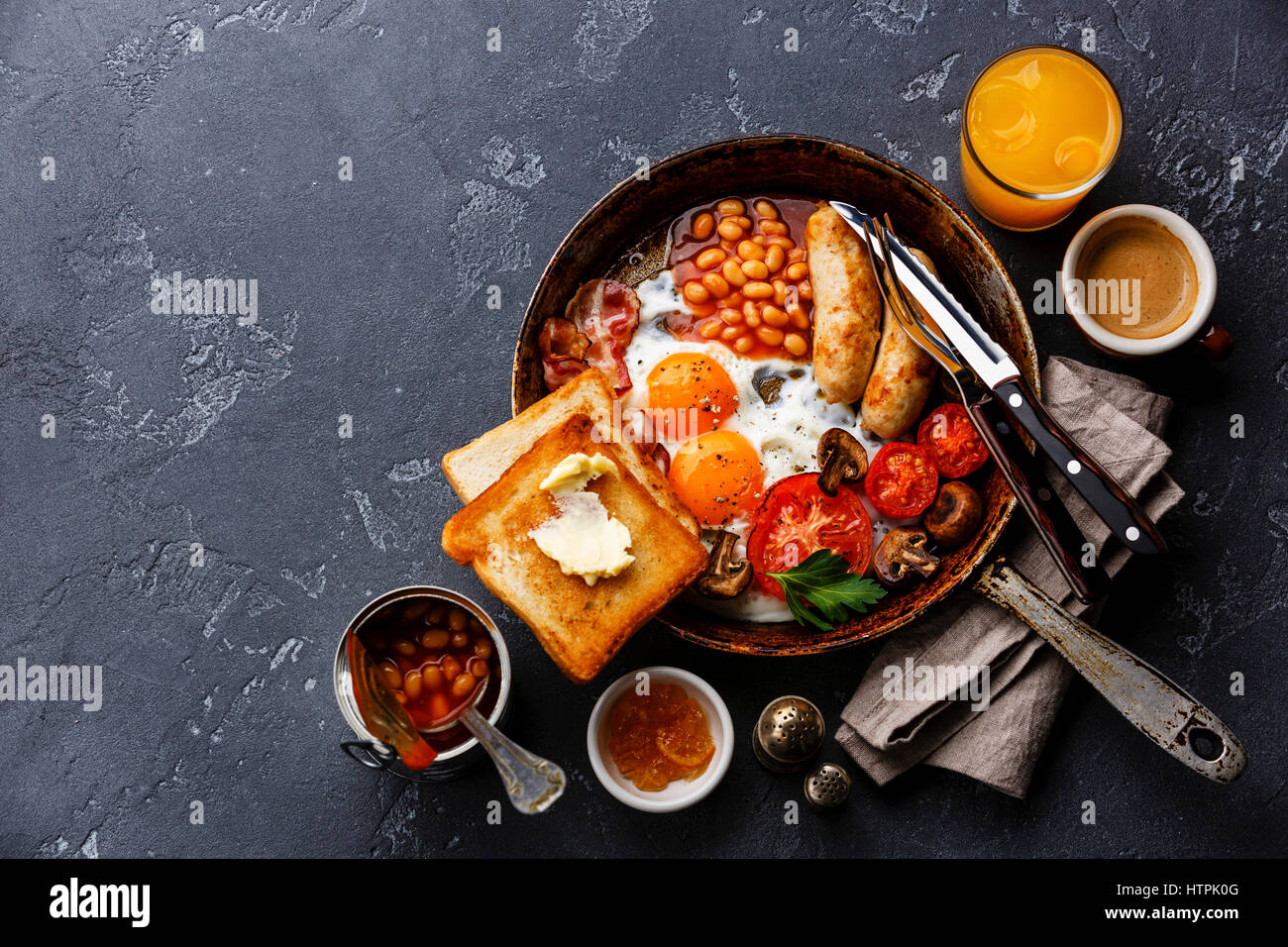 Desayuno inglés en sartén con huevos fritos, salchichas, tocino, frijoles, tostadas y café en piedra oscura espacio copia de fondo Foto de stock