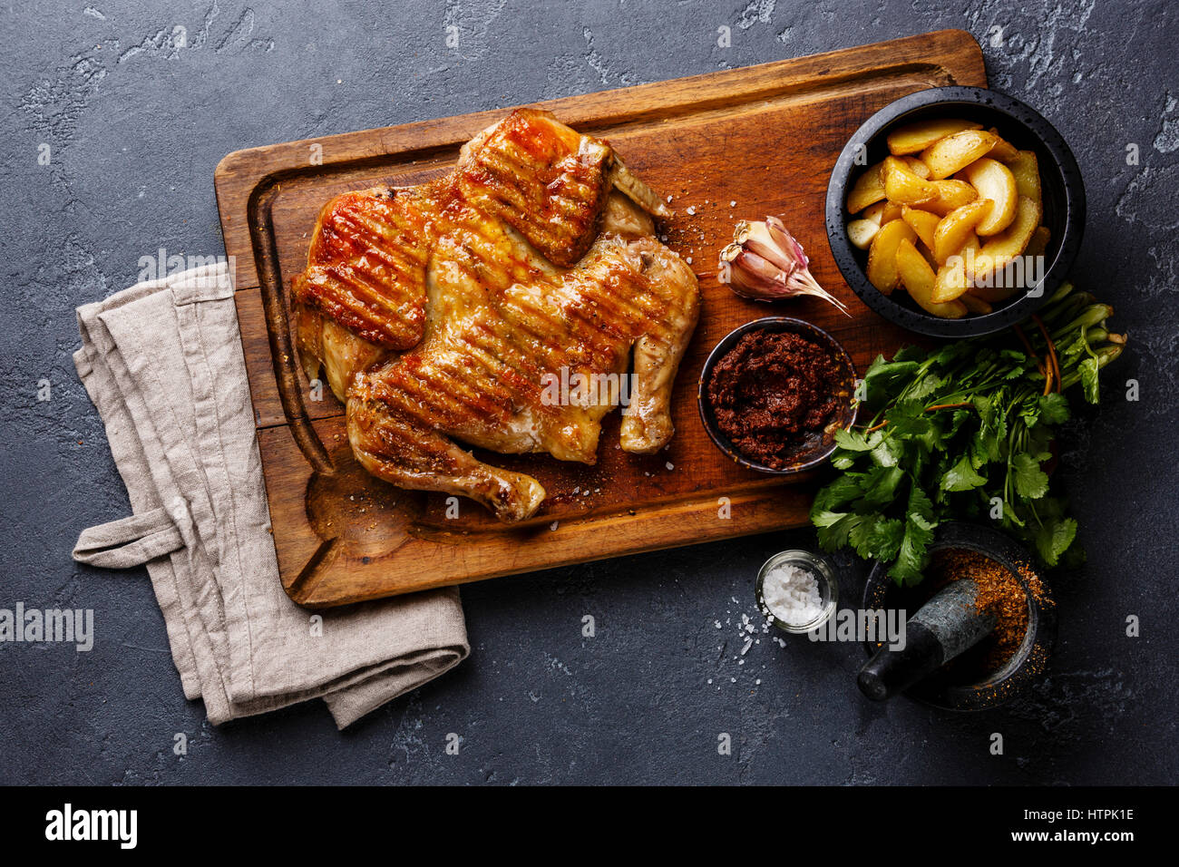 Tabaka frito a la parrilla de pollo asado y rodajas de patata en el fondo de la tabla de cortar de madera Foto de stock
