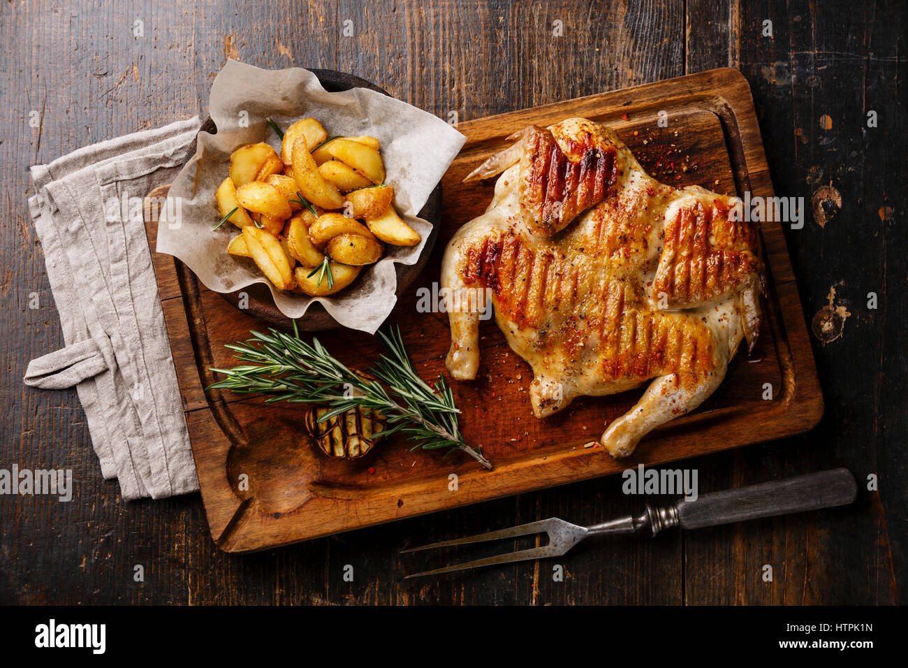Tabaka frito a la parrilla de pollo asado y rodajas de patata en el fondo de la tabla de cortar de madera Foto de stock
