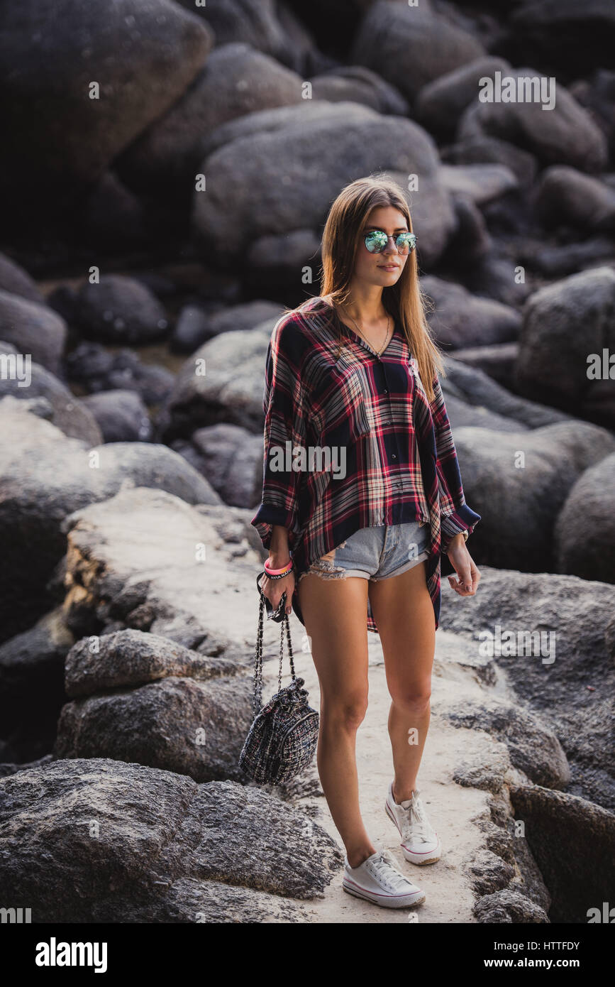 Estilo hipster mujer en camisa a cuadros y camisas en verano en la playa al  atardecer. Ruta en una de las rocas en la playa Fotografía de stock - Alamy
