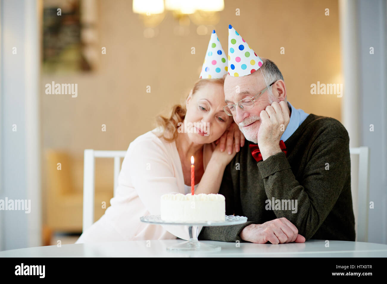 Retrato de lonely altos pareja abrazada sentados juntos a la mesa con el  pastel de cumpleaños vistiendo disfraces y mirando a vela Fotografía de  stock - Alamy