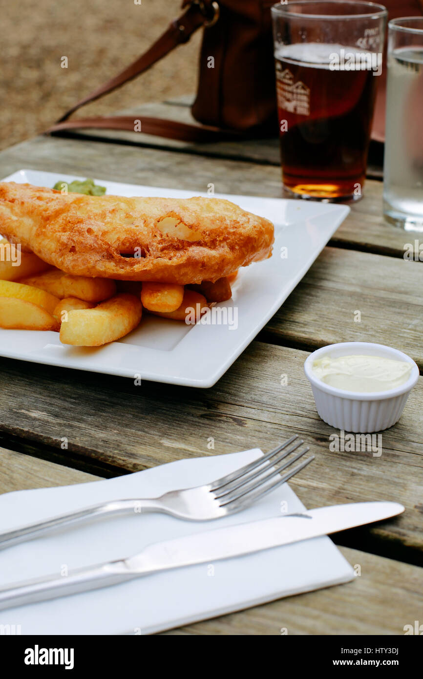 Fish and Chips, plato tradicional inglés, sobre una tabla de madera al aire libre pub, cerveza en el fondo Foto de stock
