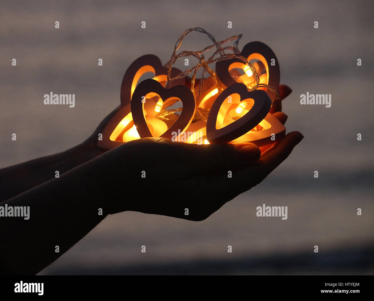 Manos de mujer sosteniendo las luces de cadena en forma de corazón Foto de stock