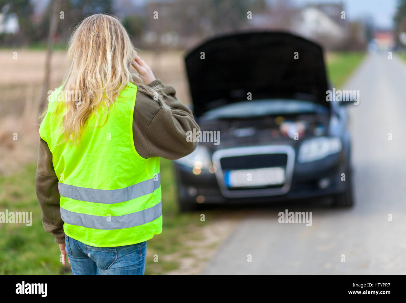 Una mujer con chaleco reflectante se levanta sobre un coche rotos Foto de stock