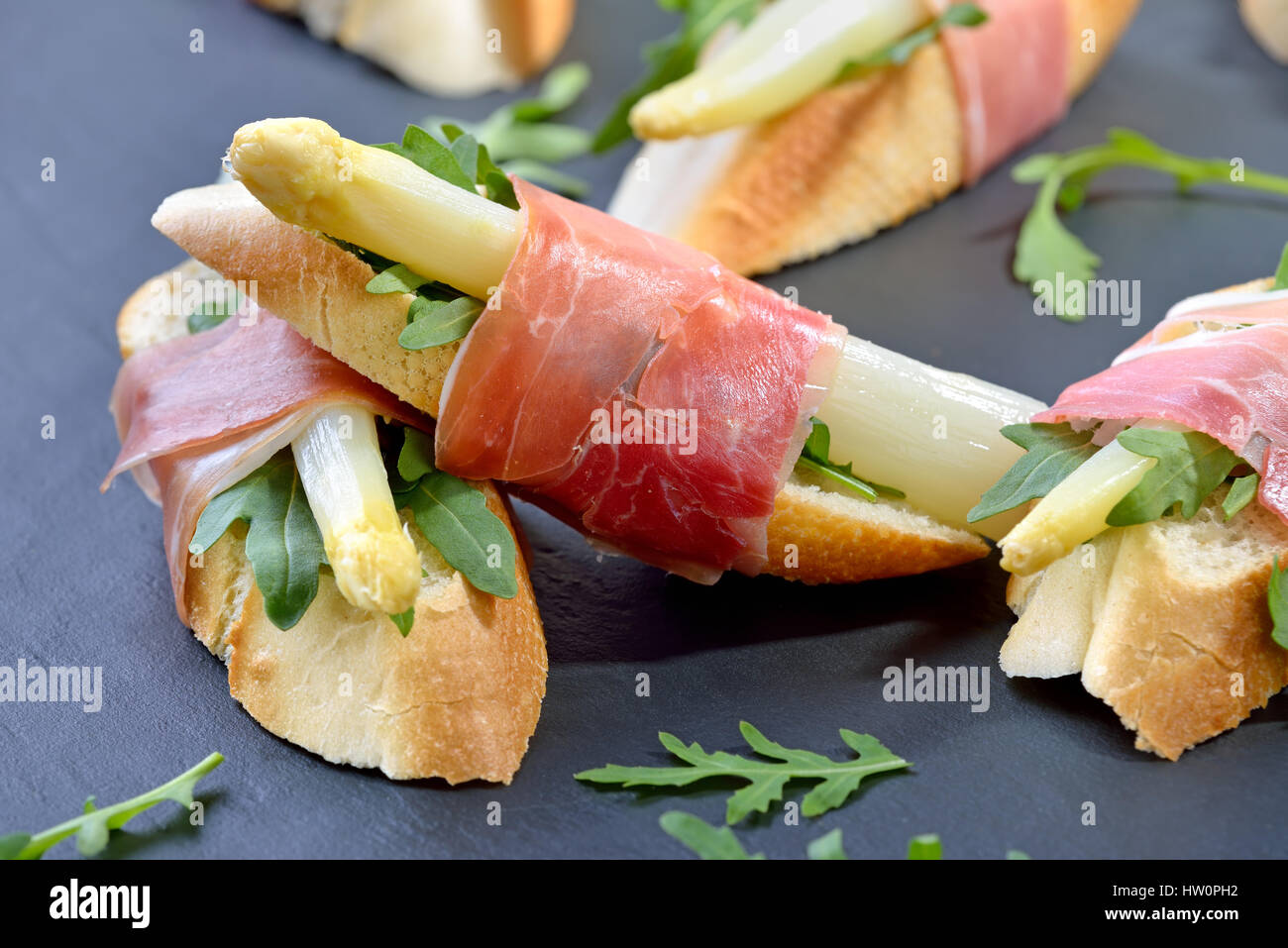 Deliciosos bocados con espárrago blanco sobre hojas de rúcula envueltos con prosciutto italiano Foto de stock