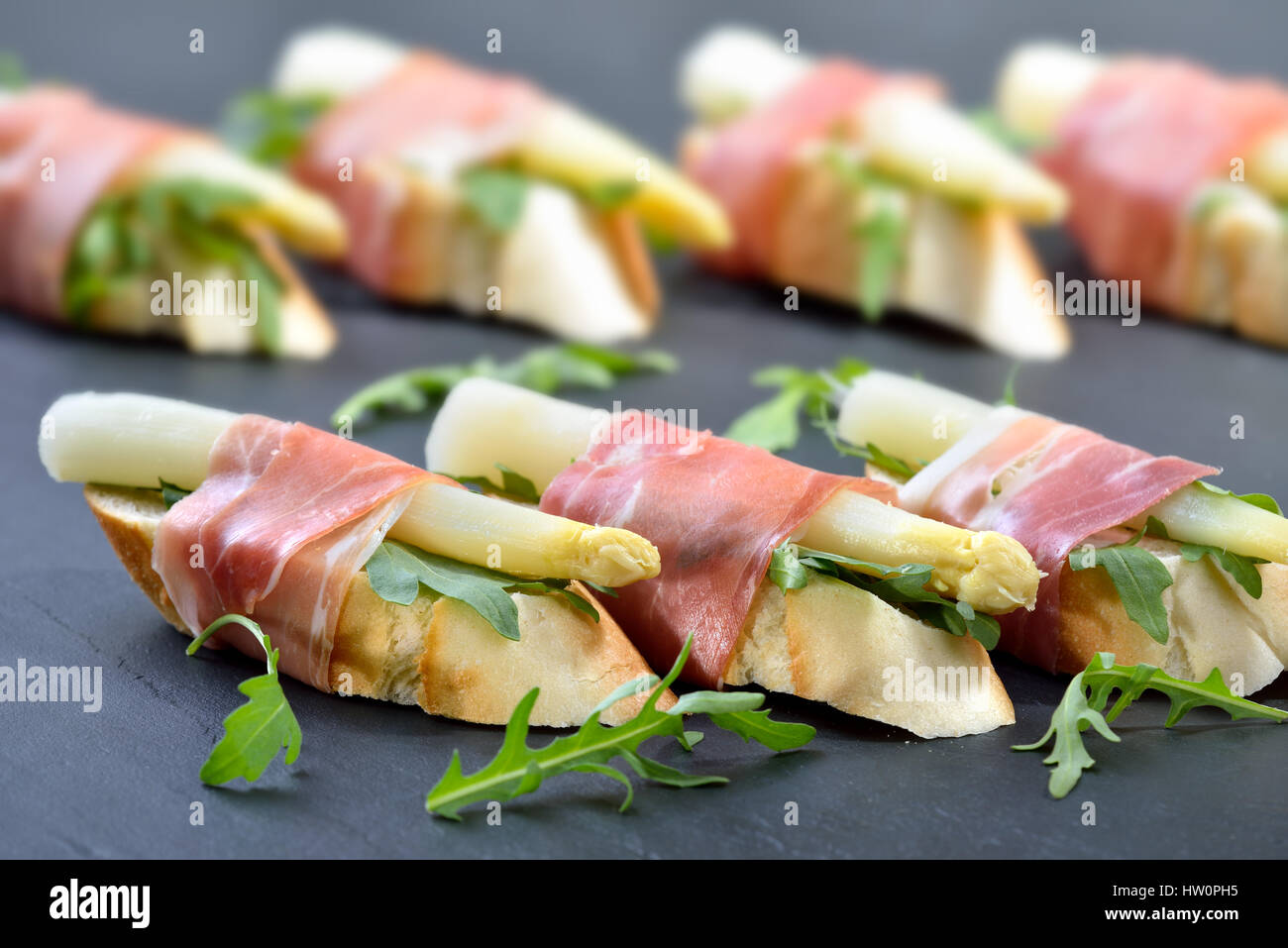 Deliciosos bocados con espárrago blanco sobre hojas de rúcula envueltos con prosciutto italiano Foto de stock