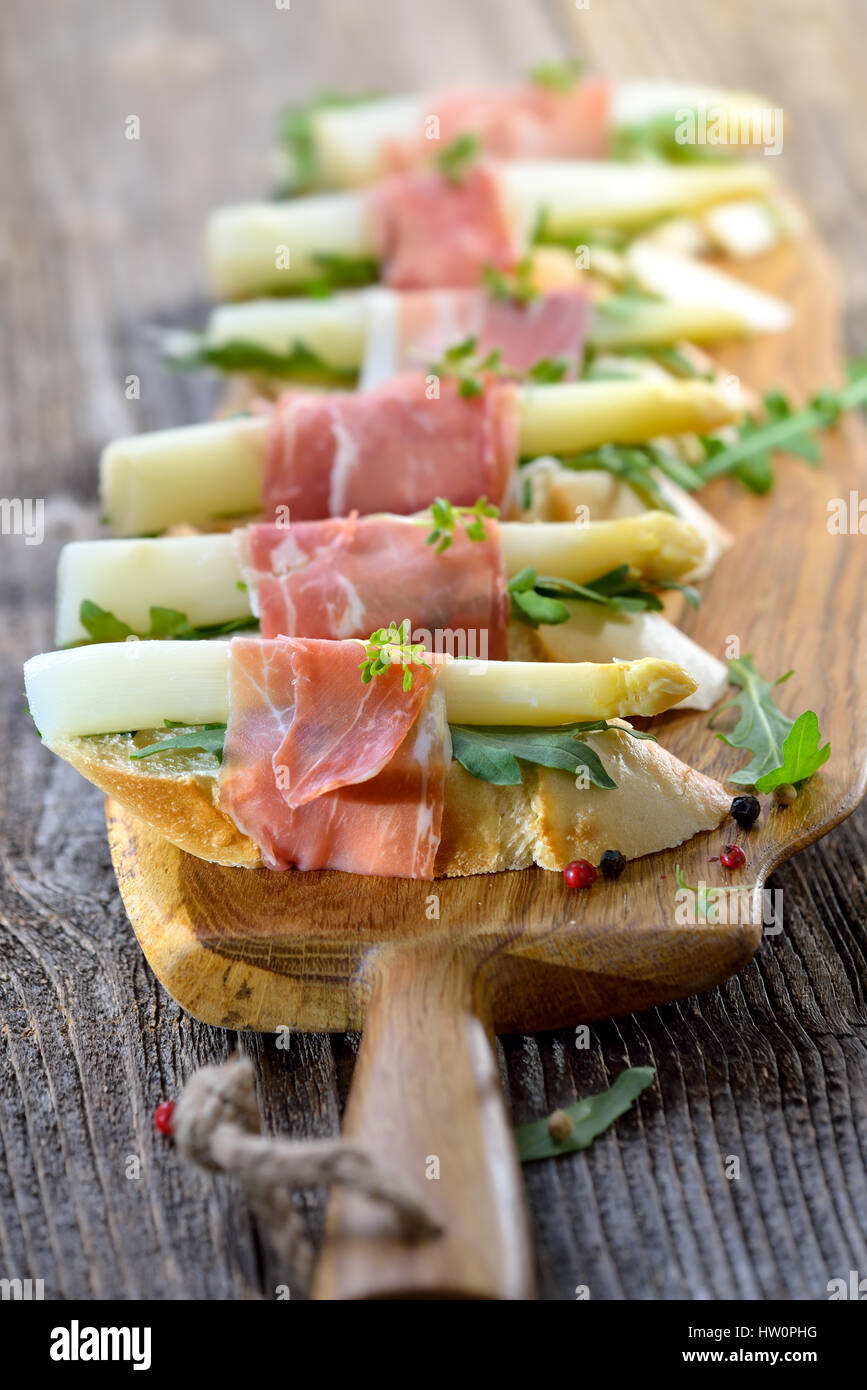 Deliciosos bocados con espárrago blanco sobre hojas de rúcula envueltos con prosciutto italiano Foto de stock