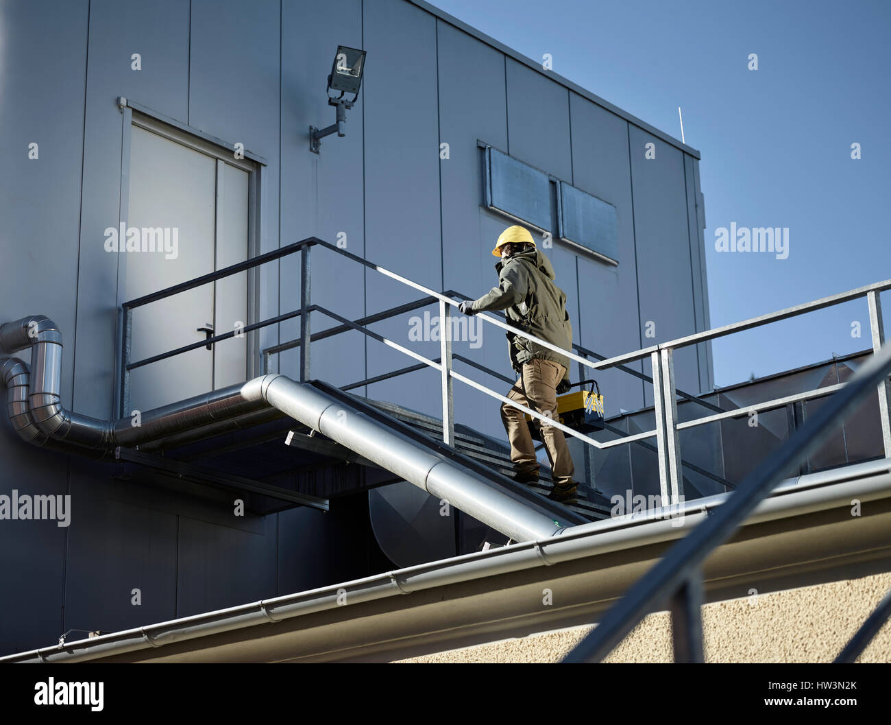 Ingeniero con casco de color amarillo y la caja de herramientas usando una escalera a una sala de máquinas, Austria Foto de stock
