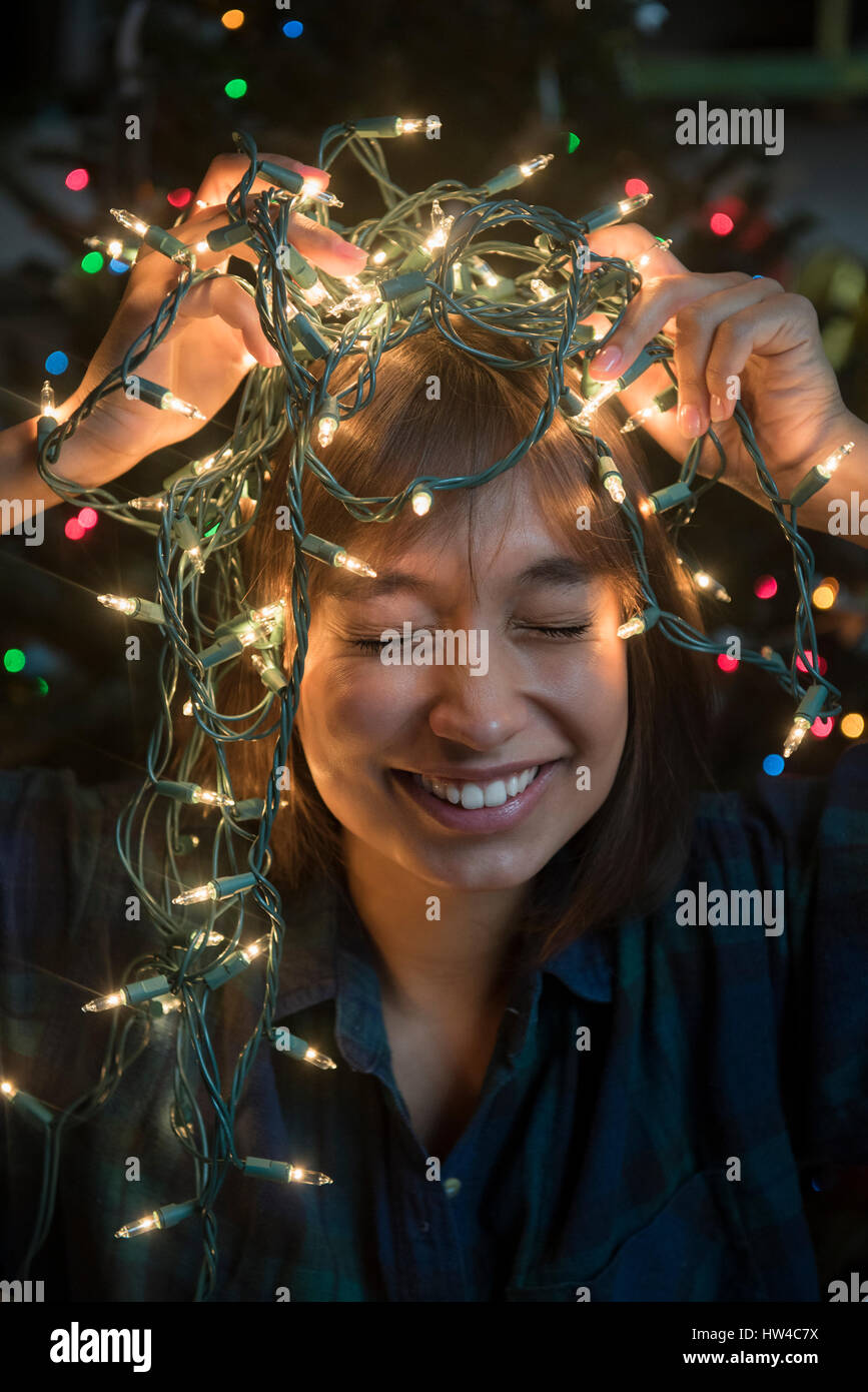 Raza mixta mujer sosteniendo las luces de cadena en la cabeza cerca del árbol de Navidad Foto de stock