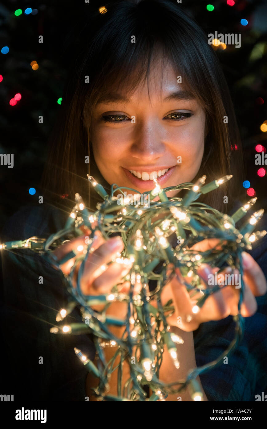 Raza mixta mujer sosteniendo las luces de cadena cerca de árbol de Navidad Foto de stock