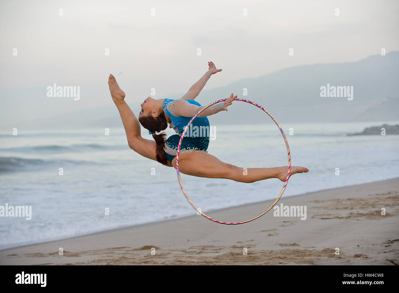 Gimnasta caucásica saltando con aro en la playa Foto de stock